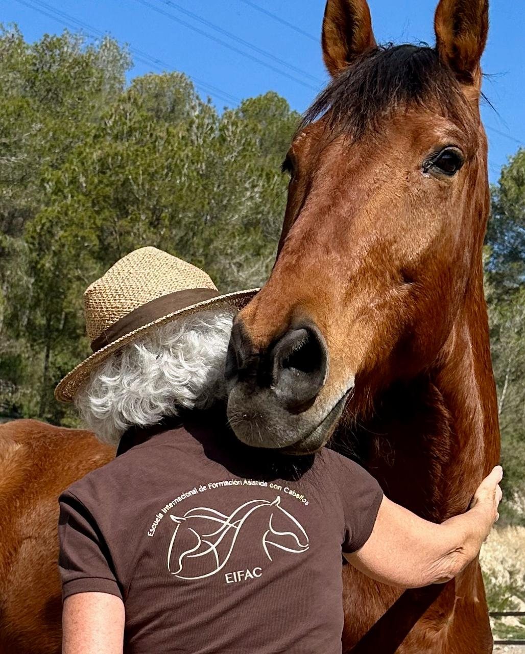 Anna Álvarez Crispi, con la camiseta de EIFAC, abraza el cuello de un caballo alazán